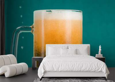 Glass of beer with foam and spray from falling ice on a turquoise green background Wall mural