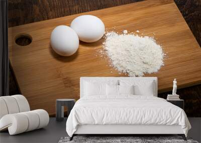 two white eggs on a wooden board and next to a handful of flour Wall mural