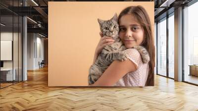 Close up portrait of the beautiful little girl with brunette loose hair the hugging her grey cat, isolated over orange background Wall mural