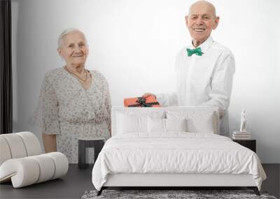 Happy elderly couple, senior man in white shirt present gift box to his old woman in white dress, celebrating birthday, isolated over white background Wall mural