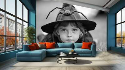 Child wearing witch hat with spider design lying on grass Wall mural