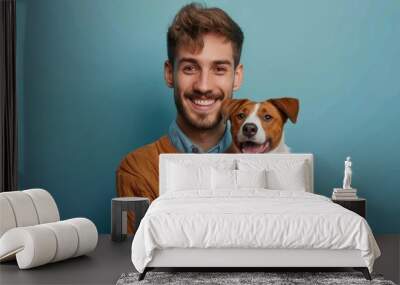 Smiling young man holding adorable jack russell terrier against blue background Wall mural