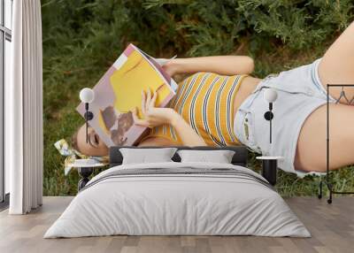 Young woman reading magazine lying on grass Wall mural