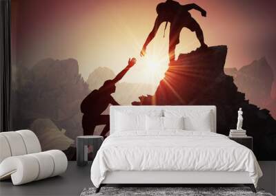 Help and assistance concept. Silhouettes of two people climbing on mountain and helping. Wall mural