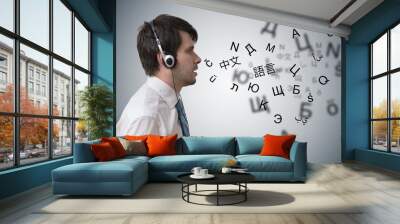 Young man with headphones is learning different foreign languages. Wall mural