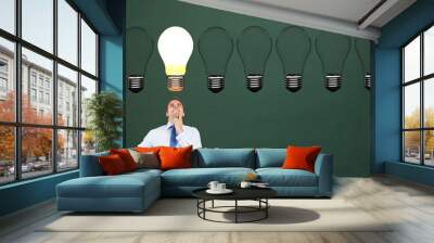 Businessman looking at glowing bulb against green background Wall mural