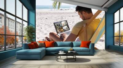 Caucasian man on holidays using laptop with views of home from security cameras on screen Wall mural