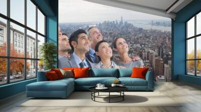 Composite image of group of businesspeople looking above against aerial view of cityscape Wall mural