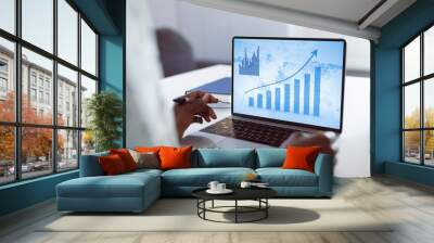 Hands of african american businesswoman at desk using laptop with blue graphs on screen Wall mural