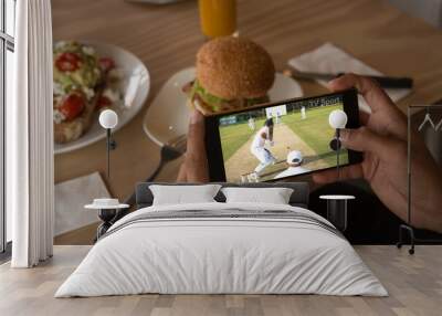 Hands of caucasian man at restaurant watching cricket match on smartphone Wall mural