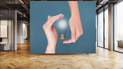 Light bulb between two hands with blue background Wall mural