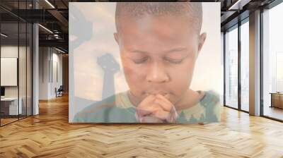 Multiple exposure of african american elementary boy praying with cemetery crosses against sky Wall mural