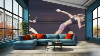 Two diverse female athletes holding baton running against grey background Wall mural