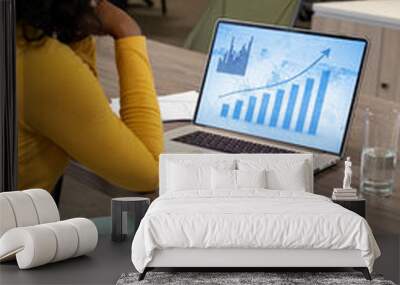 Vertical of biracial businesswoman using laptop in empty office with graphs and data on screen Wall mural