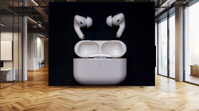 White wireless headphones with a charging case on a black background. Wall mural