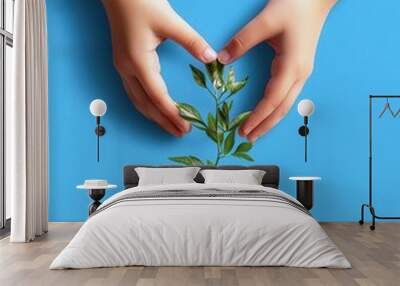 Two hands gently supporting a small potted plant against a vibrant blue background, symbolizing care and growth. Wall mural