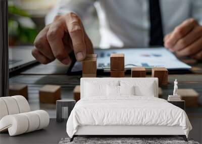 A businessman sitting at a desk, building with wooden cubes to symbolize strategic thinking and planning. Wall mural