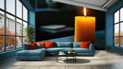 A candle is lit and is sitting on a table. The candle is yellow and the light is shining on it. Scene is calm and peaceful Wall mural