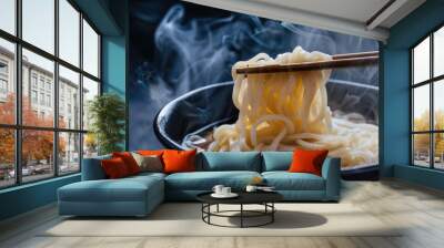 A delicious bowl of noodles with chopsticks, served in a black bowl. The meal is steaming hot and ready to eat. Wall mural