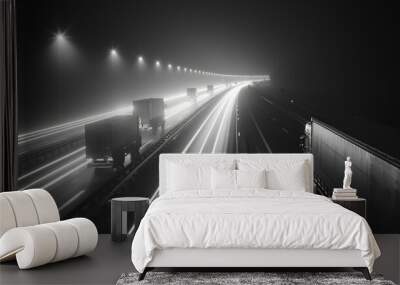 A highway with a long line of semi trucks driving down it. The image is in black and white and the mood is somber Wall mural