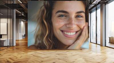 A joyful young woman with freckles smiling at the camera, suggesting a carefree and happy moment. Wall mural