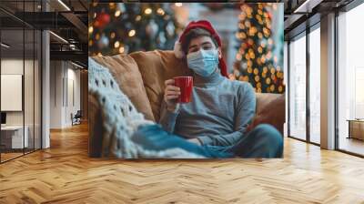 A man wearing a red santa hat and a face mask is sitting on a couch with a cup of coffee Wall mural