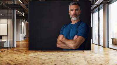 A man with a beard and gray hair is wearing a blue shirt and standing with his arms crossed Wall mural