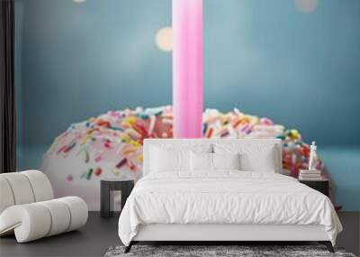 A pink frosted doughnut with sprinkles on top and a lit candle in the center. Concept of celebration and joy, as it is a birthday cake Wall mural