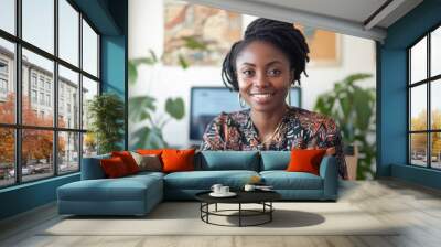 A woman with a smile on her face is sitting at a desk with a laptop and a potted plant in the background Wall mural