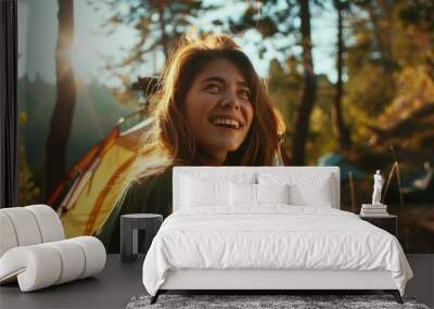 A woman with long brown hair is smiling and sitting in front of a yellow tent. The scene is set in a forest, and the woman is enjoying her time outdoors Wall mural