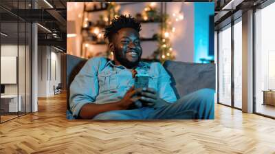 Man is sitting on couch and smiling while holding cell phone Wall mural