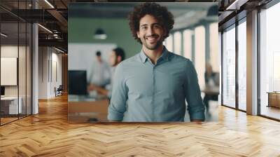 Man with curly hair is smiling in front of group of people in office Wall mural