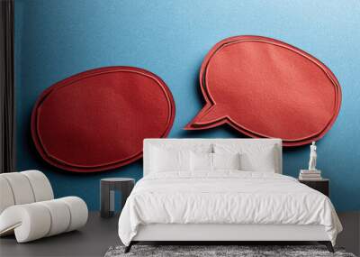 Two red paper cutouts of speech bubbles are on blue background Wall mural