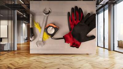 A wrench a utility knife a tape measure and work gloves lay on a metal surface Wall mural