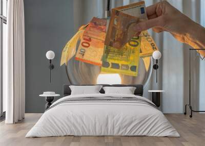 Euro bills over glowing lamp and a woman hand holding Euro banknote. Electricity cost, electricity bill payment, expensive energy concept Wall mural