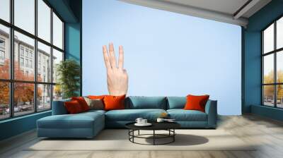 Female hand shows number three. Woman hand showing three fingers, pointing fingers up on light blue background Wall mural