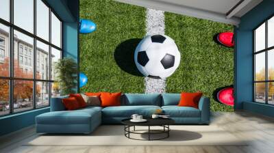 Soccer football background. Soccer ball and two pair of football sports shoes on artificial turf soccer field with shadow from football goal net on sunny day outdoors. Top view Wall mural