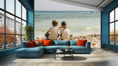 Two boys sitting together on the beach and looking at sea, boats, yachts. Sunny day. Back view. Holiday concept Wall mural