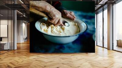 hands of an old woman with a wooden spoon, whip homemade butter with whey Wall mural