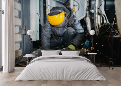 man worker in a uniform and a mask works with a grinder, cuts metal for a truck body repair. Wall mural