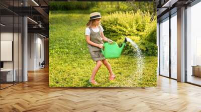 Farmer girl in summer straw hat. Little gardener farming spinning, having fun in garden with big green watering can water fresh grass. Harvest help work. Cultivation healthy organic food, countryside Wall mural