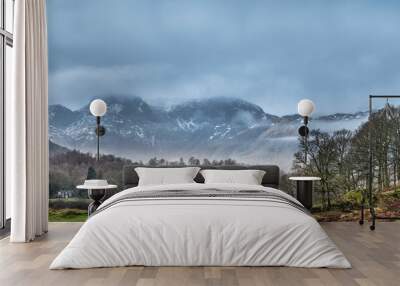 Epic dramatic landscape image of view from Elterwater across towards Langdale Pikes mountain range on foggy Winter morning Wall mural