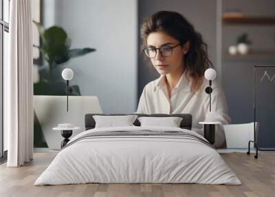 Photograph of a young woman with a determined look, working on her business plan, writing on her laptop in her minimalist studio Wall mural