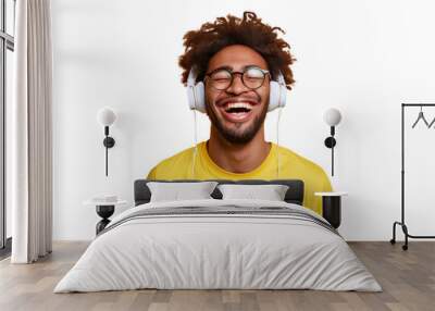 Young ethnic man with glasses wearing headphones and a yellow t-shirt, laughing , Isolated on white background Wall mural