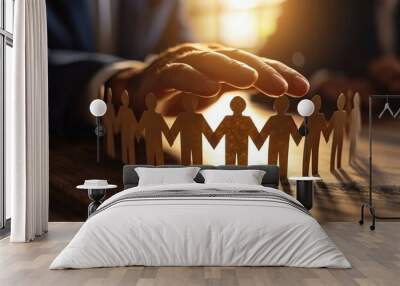 close-up shot of a businessman's hand protecting a group of paper figures on his desk in the office, symbolizing teamwork and security. Wall mural