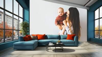 Happy mother holding up her baby girl. Young beautiful mother holds her baby and cuddles, motherhood concept Wall mural