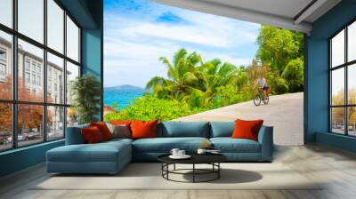 happy young guy riding a bike on the road by the sea in the seychelles. concept of vacation and acti Wall mural