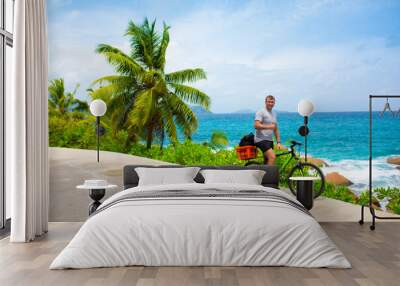 Happy young guy riding a bike on the road by the sea in the Seychelles. Concept of vacation and active lifestyle. Cycling. The man on the bike. Wall mural