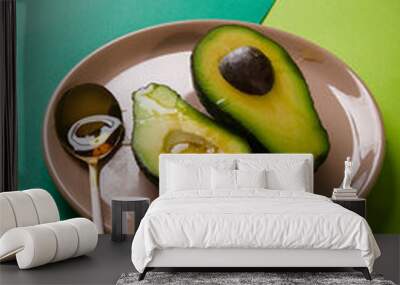 Two slices of avocado on pink plate with a spoon on green abstract geometric background, copy space Wall mural