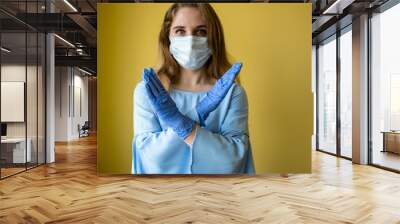 a young beautiful woman with long hair wearing a medical mask and protective disposable gloves on a bright yellow background. Epidemic and quarantine due to coronavirus, self-isolation and treatment Wall mural